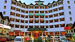 Un hotel de varios pisos con entrada central, balcones y diversas tiendas en la planta baja.