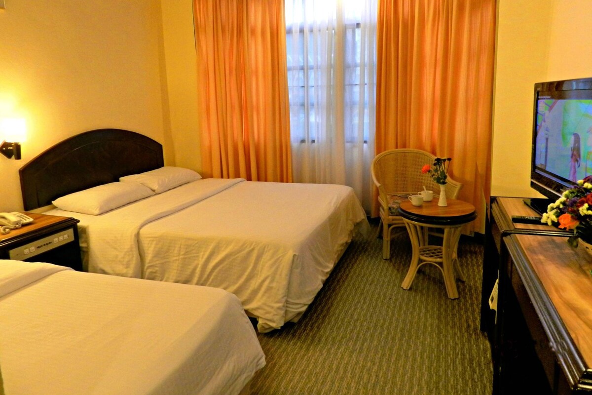 Une chambre d’hôtel avec deux lits, une télévision, un bureau avec une chaise et une fenêtre avec des rideaux.