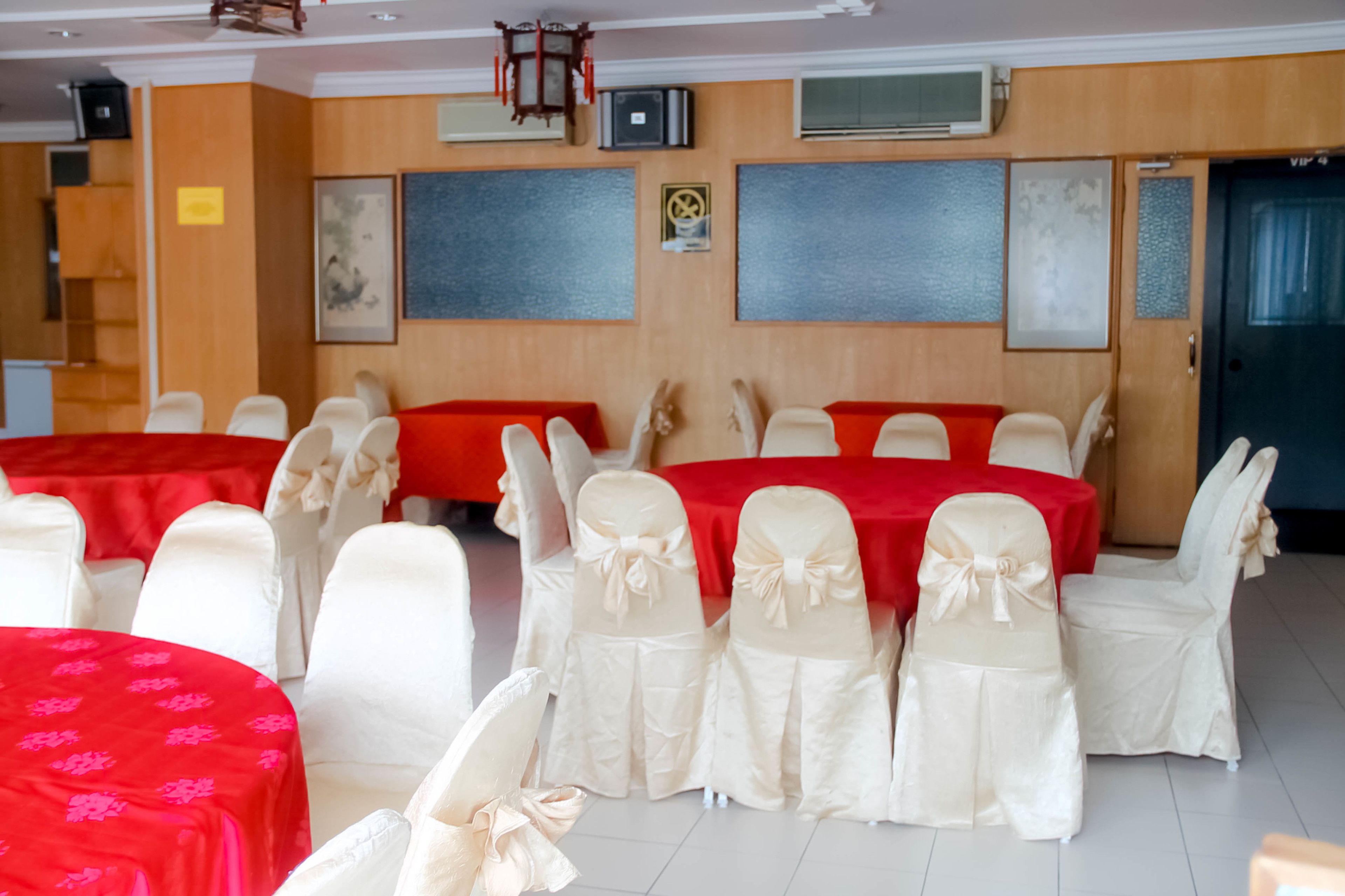 Une salle de banquet avec des tables rondes recouvertes de nappes rouges et des chaises blanches ornées de nœuds.
