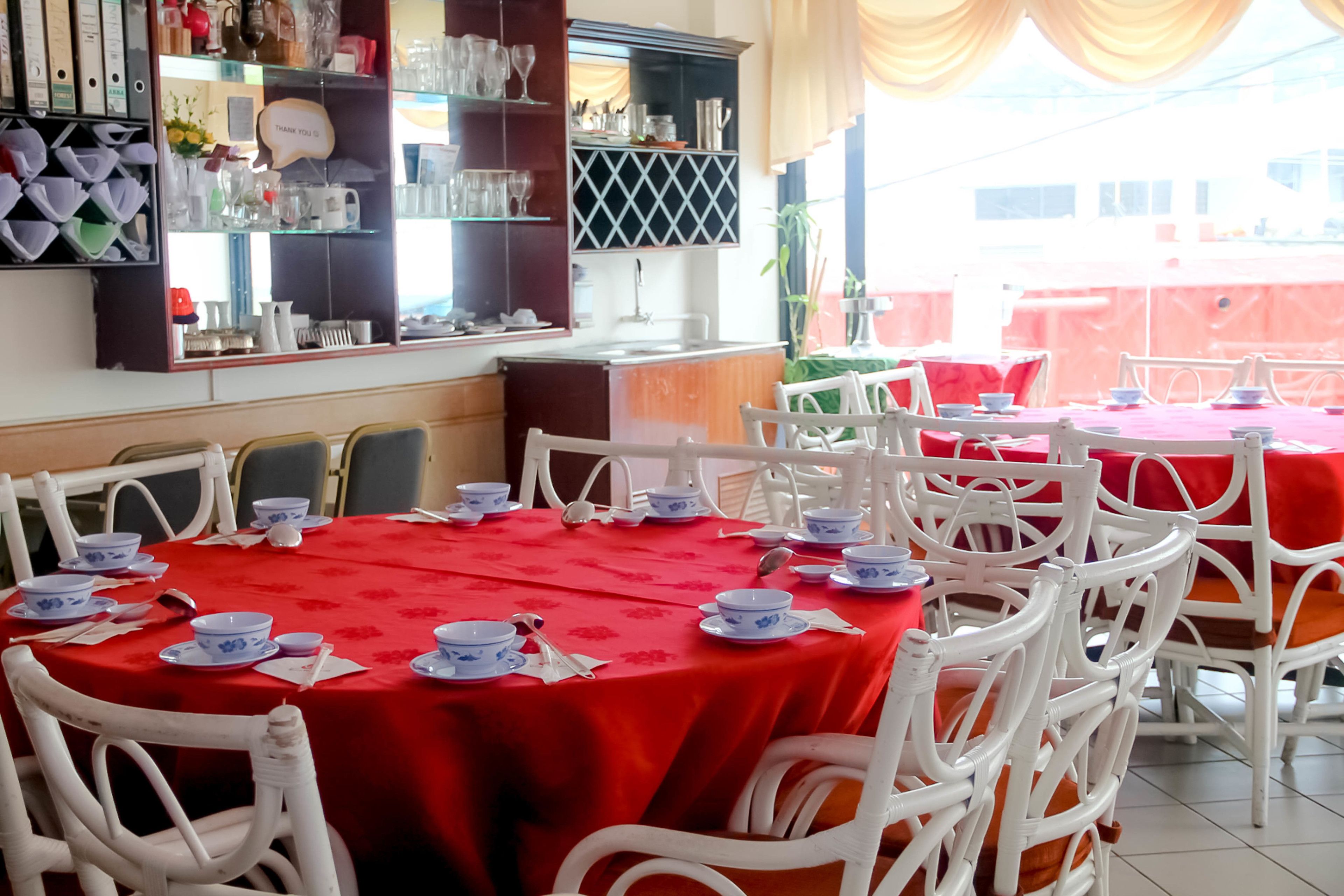 Un espace repas avec des tables rondes recouvertes de nappes rouges, des chaises blanches et de la vaisselle bleue et blanche.