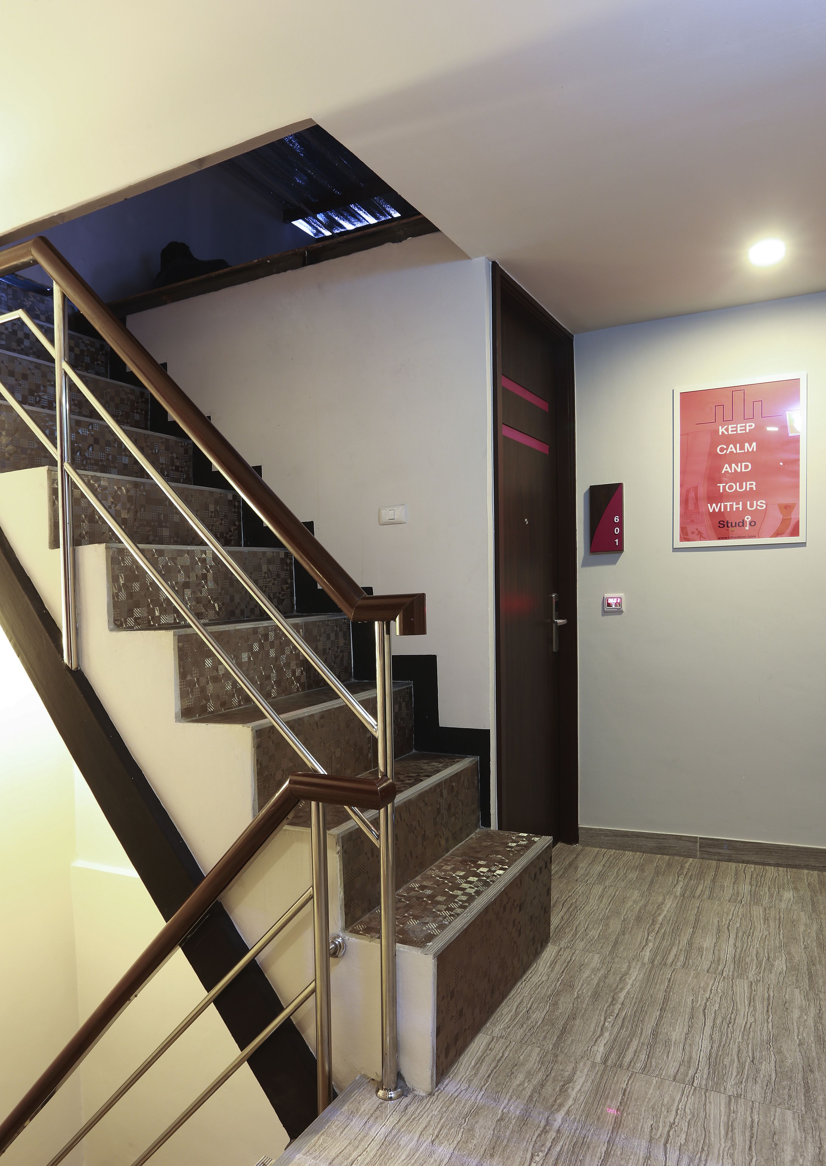 A modern staircase with metal railings and a wooden handrail, leading to a landing with a red sign.