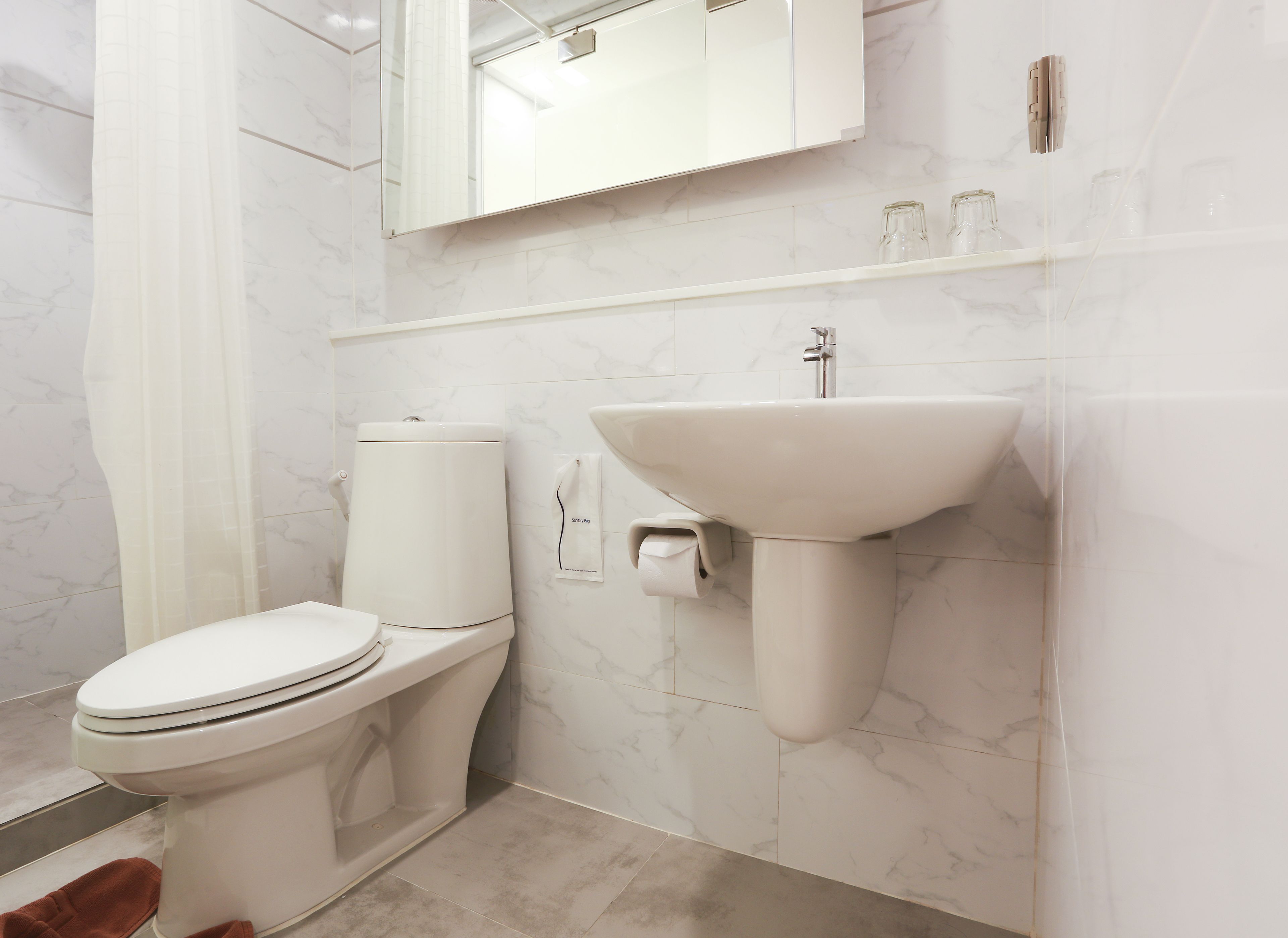 A modern bathroom with a toilet, sink, and marble-tiled walls.