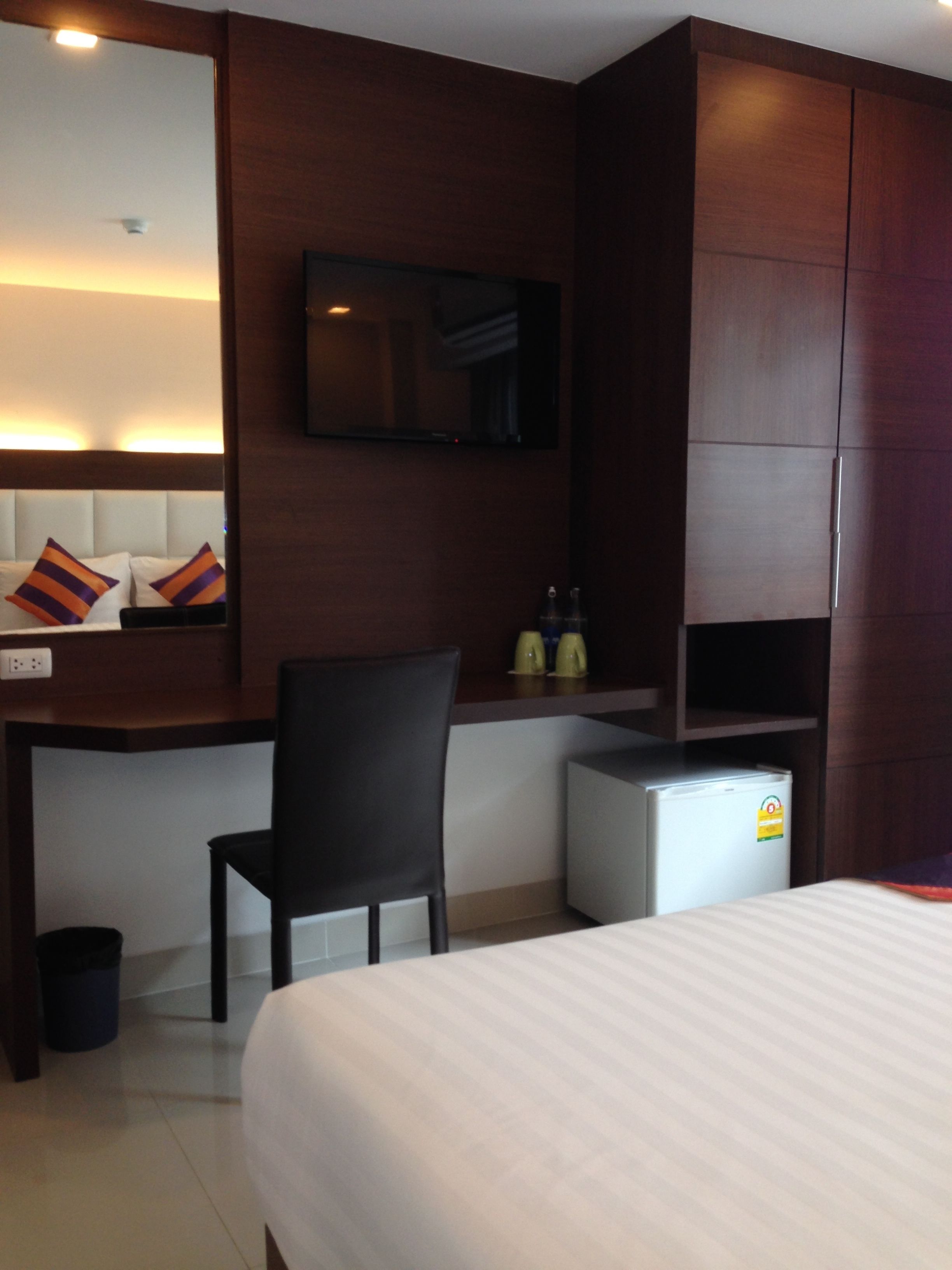 A hotel room with a bed, a desk, a chair, a television mounted on the wall, and a small refrigerator.