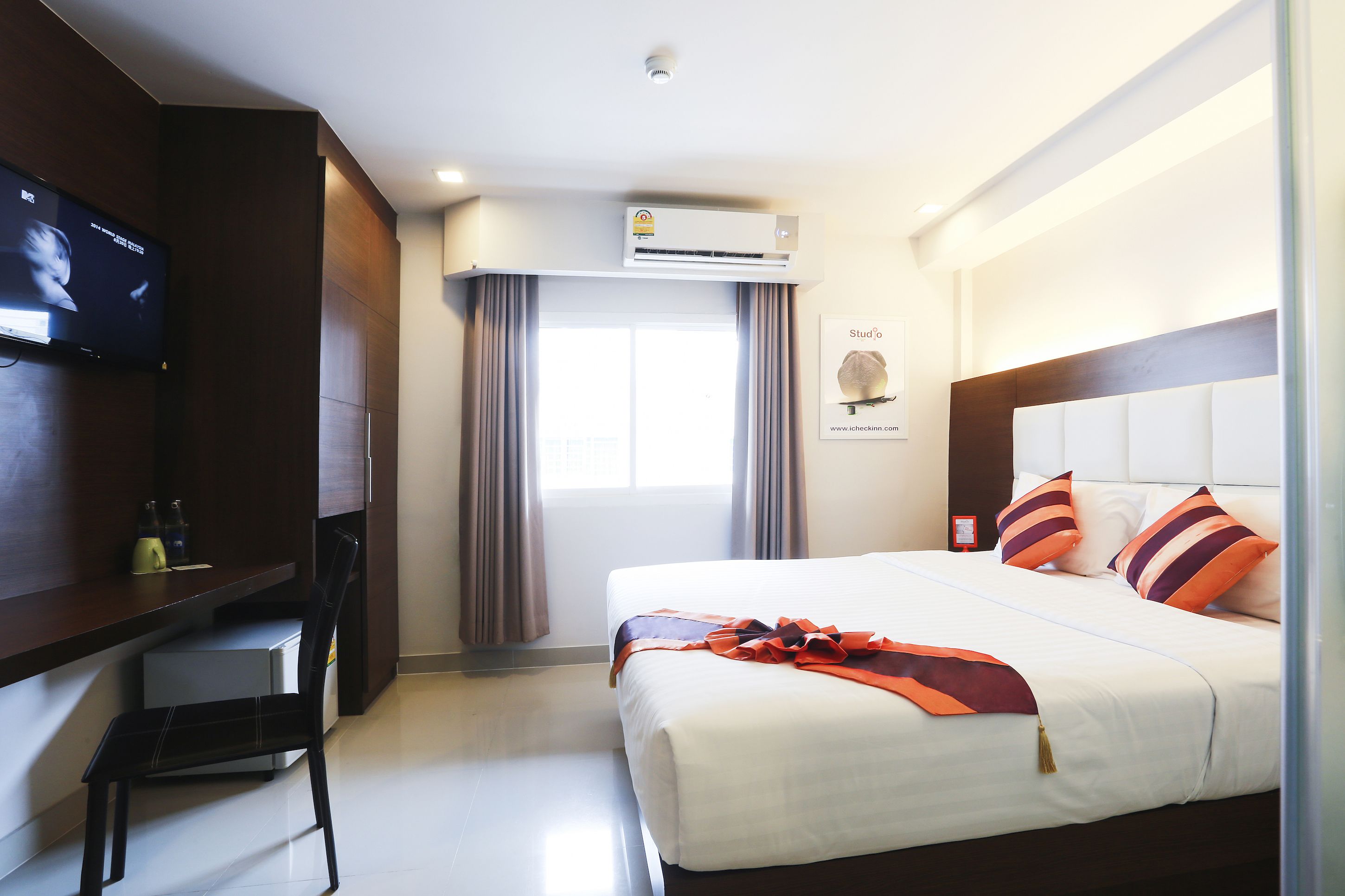 Habitación de hotel con cama, escritorio, televisor, aire acondicionado y ventana con cortinas.