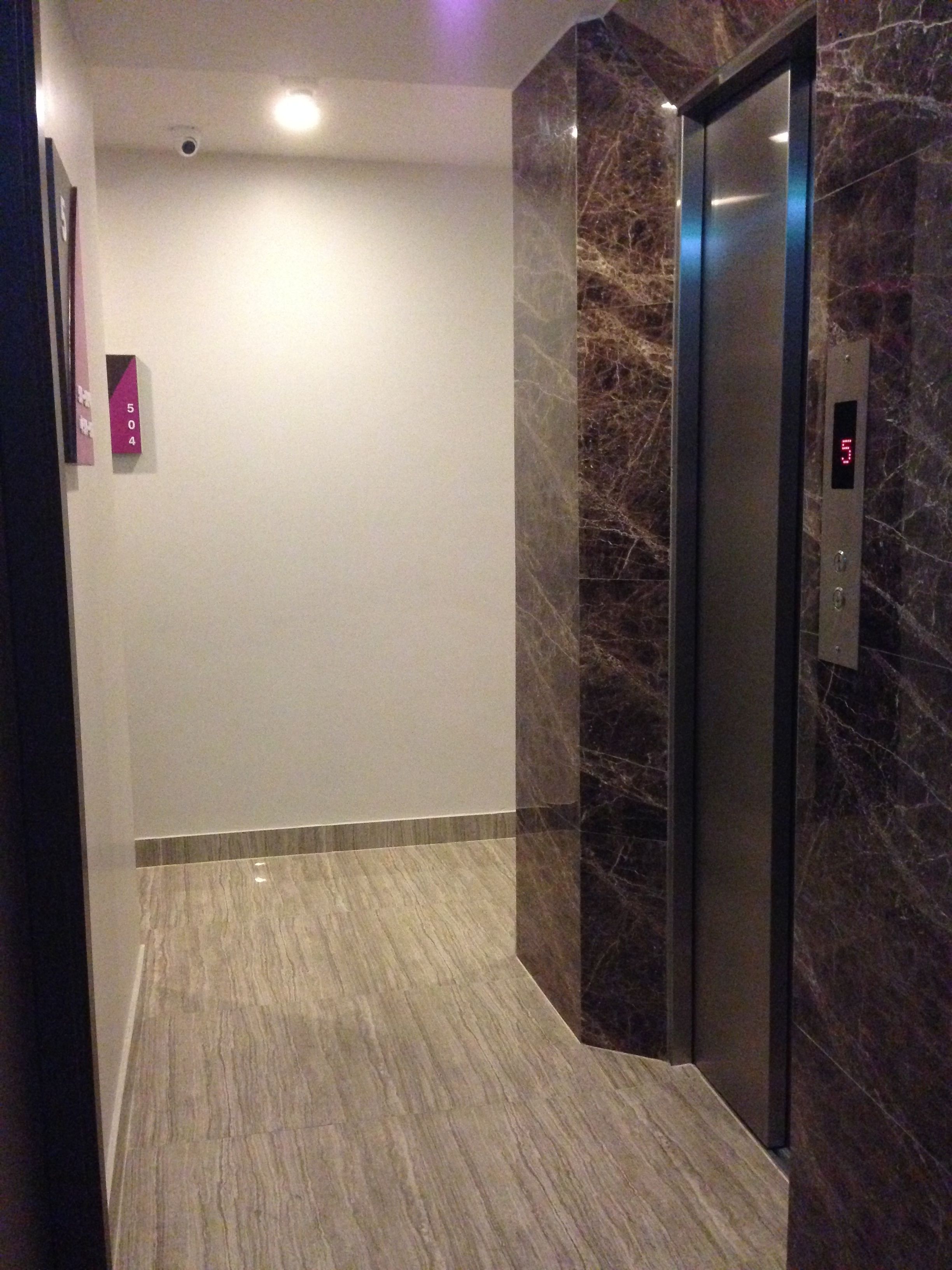 An elevator with a digital display, marble walls, and a tiled floor.