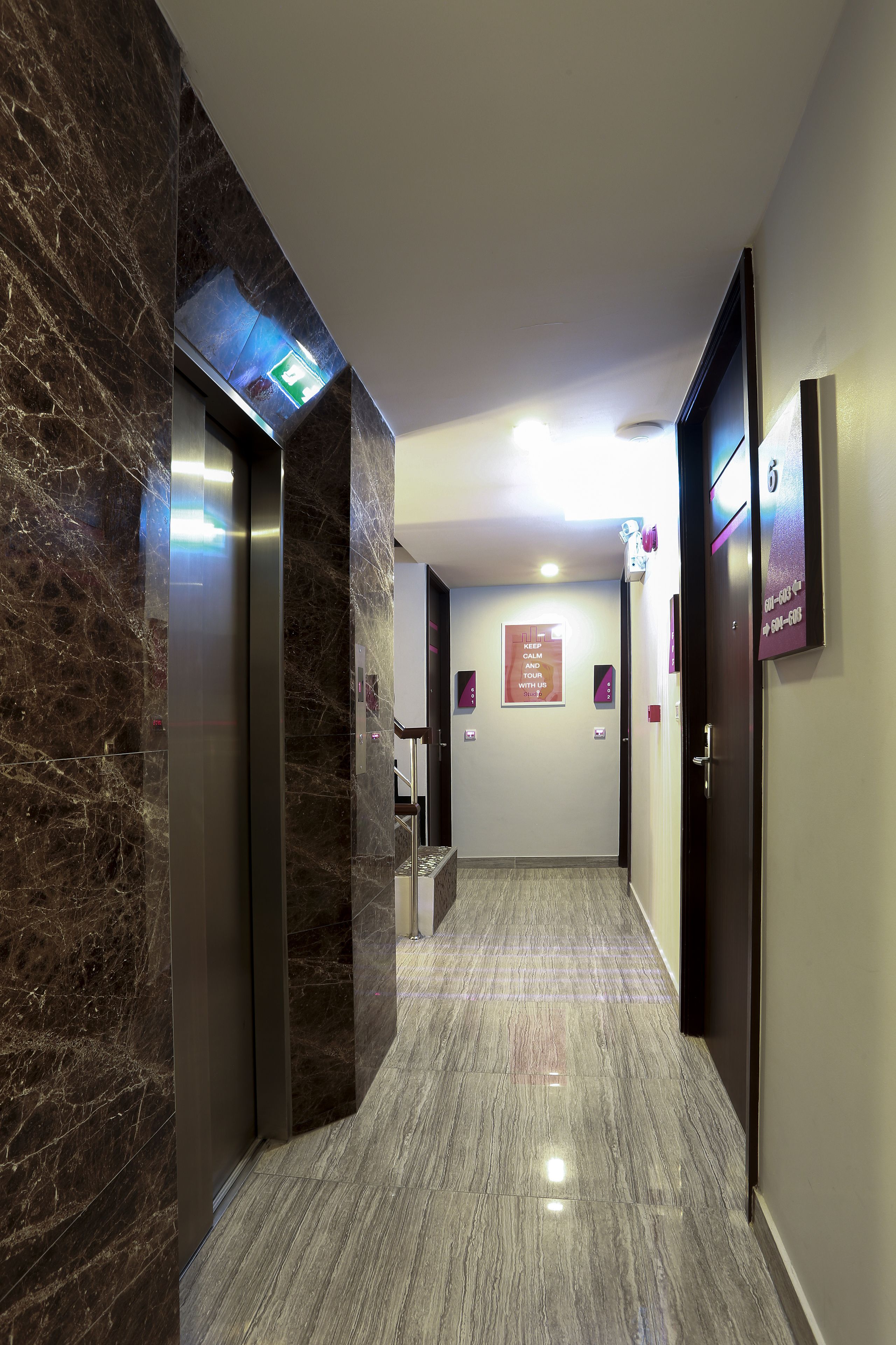 Un pasillo moderno de hotel con paredes de mármol, piso pulido y un ascensor central.