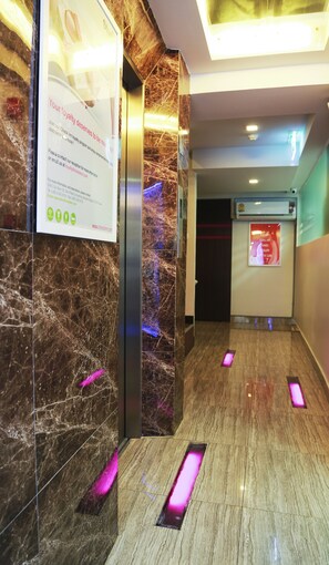 A modern hotel lobby with a marble wall, a reception desk, and a digital screen displaying a message. - Studio Nana (Bangkok)