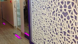 A modern hotel corridor with a decorative white panel, a glass door, and a purple accent wall. - Studio Nana (Bangkok)