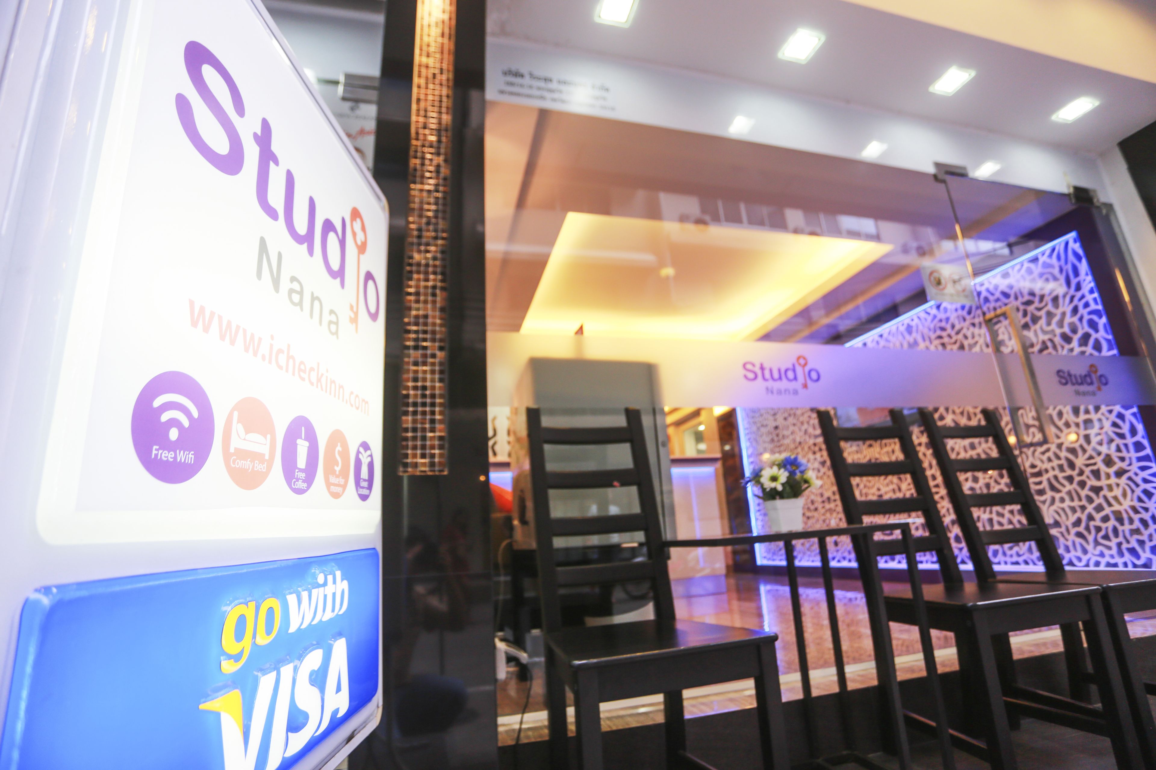 Un letrero de Studio Nanna con el logotipo 'go with VISA', puerta de vidrio de acceso y un interior moderno con sillas y mesas.