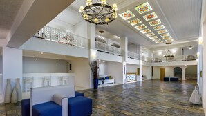 A spacious lobby with a high ceiling, patterned stone flooring, and a central seating area with blue sofas. - Hotel Amalia (Skopelos)