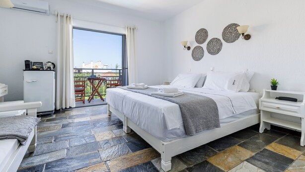 A modern hotel room with a large bed, a small desk, and a balcony with a view. - Hotel Amalia (Skopelos)