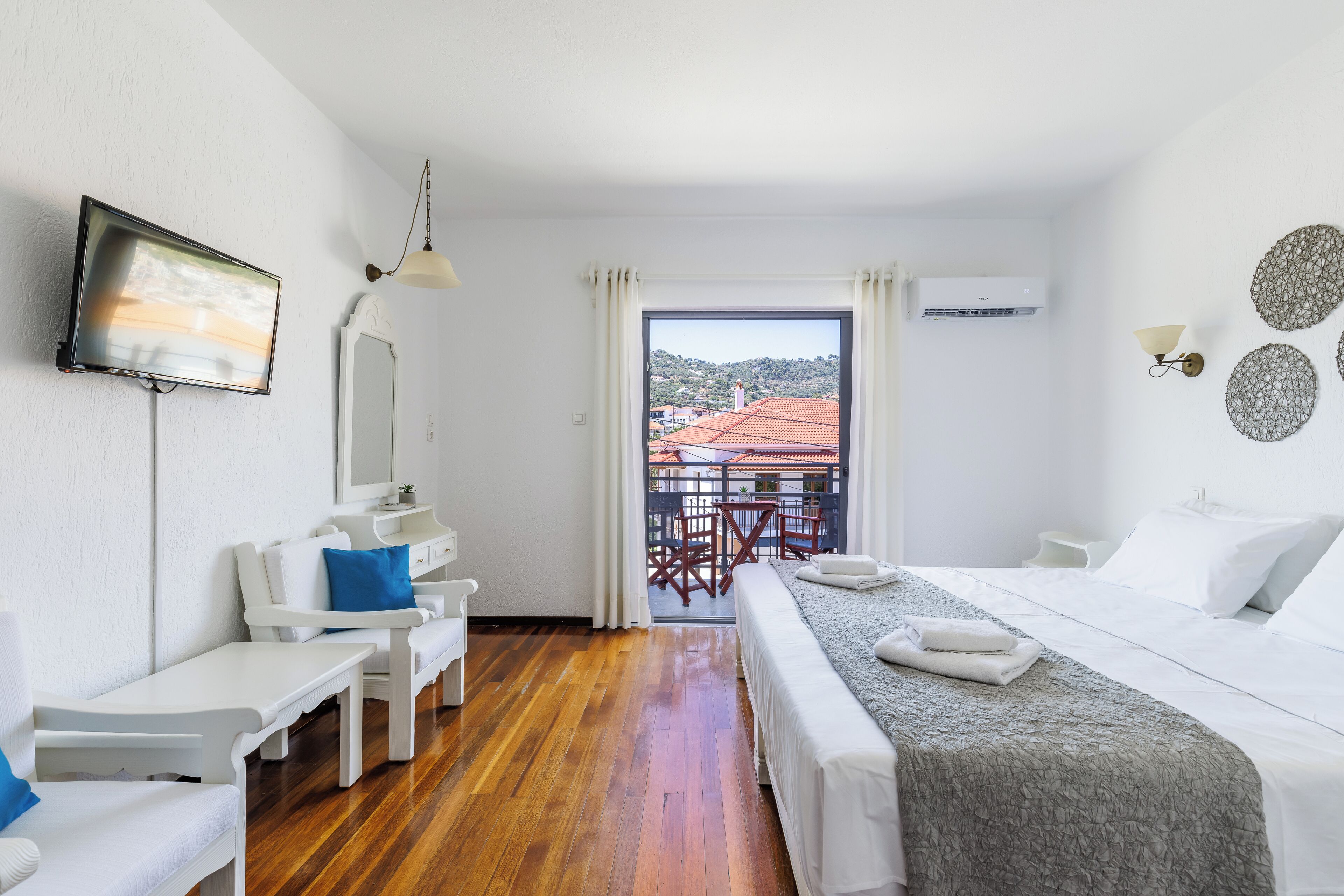 Habitación de hotel con cama, escritorio, silla, televisión y balcón con vistas a edificios.