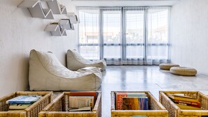 A modern living room with a sofa, a bookshelf, and wicker baskets on the floor. - Hotel Amalia (Skopelos)