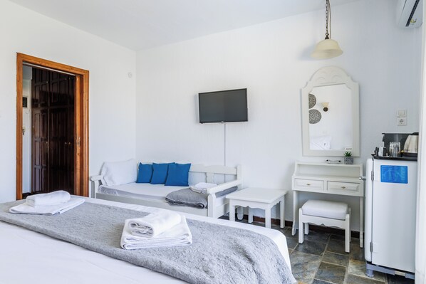 A hotel room with a bed, a desk, a chair, a television, and a refrigerator.