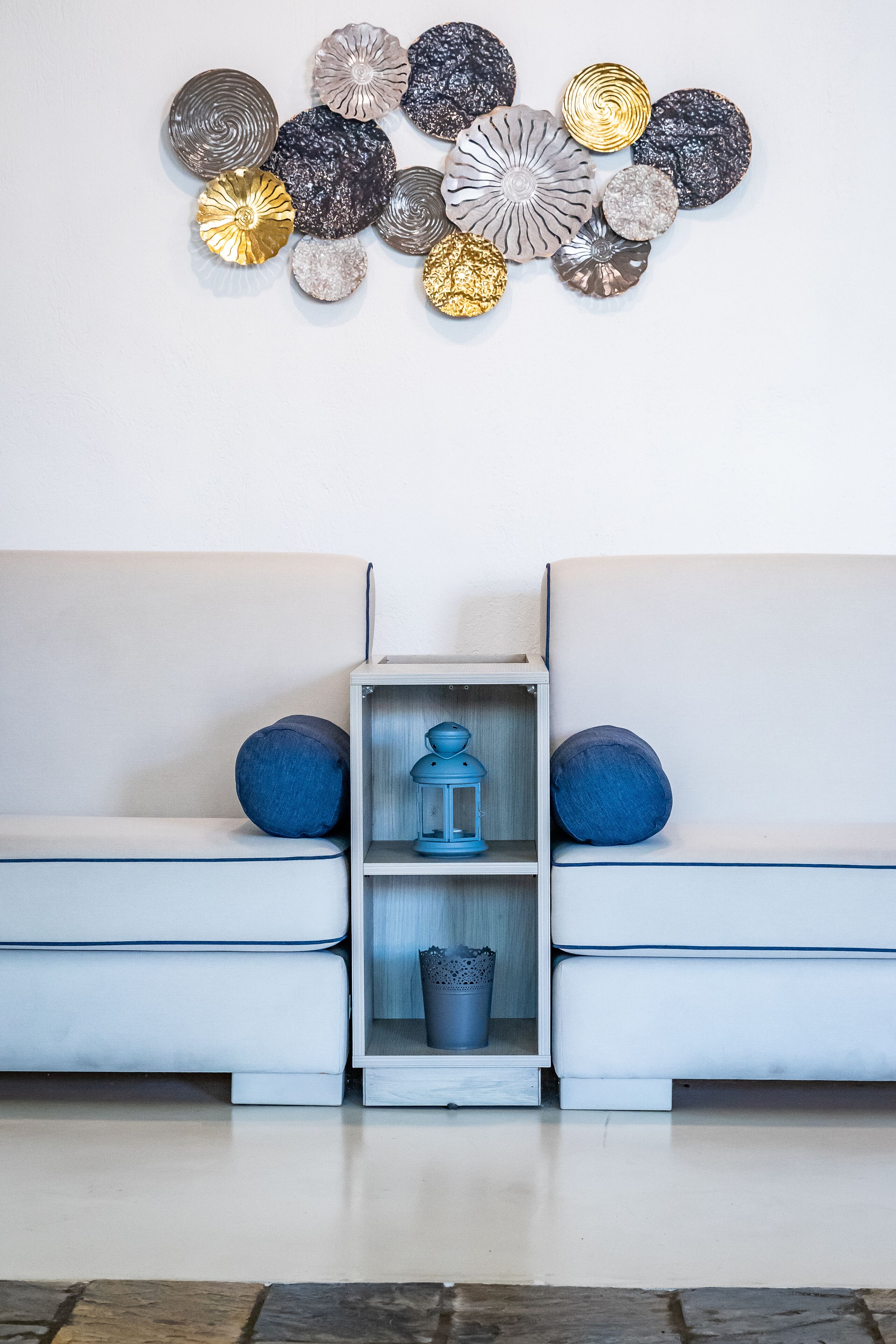 Un soggiorno moderno con un divano bianco, due cuscini blu, un tavolino in legno con una lanterna blu e un'opera d'arte decorativa sulla parete.