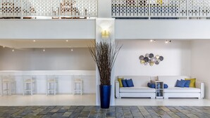 A spacious lobby with a high ceiling, a central decorative column, a seating area with a sofa and chairs, and a patterned stone floor. - Hotel Amalia (Skopelos)