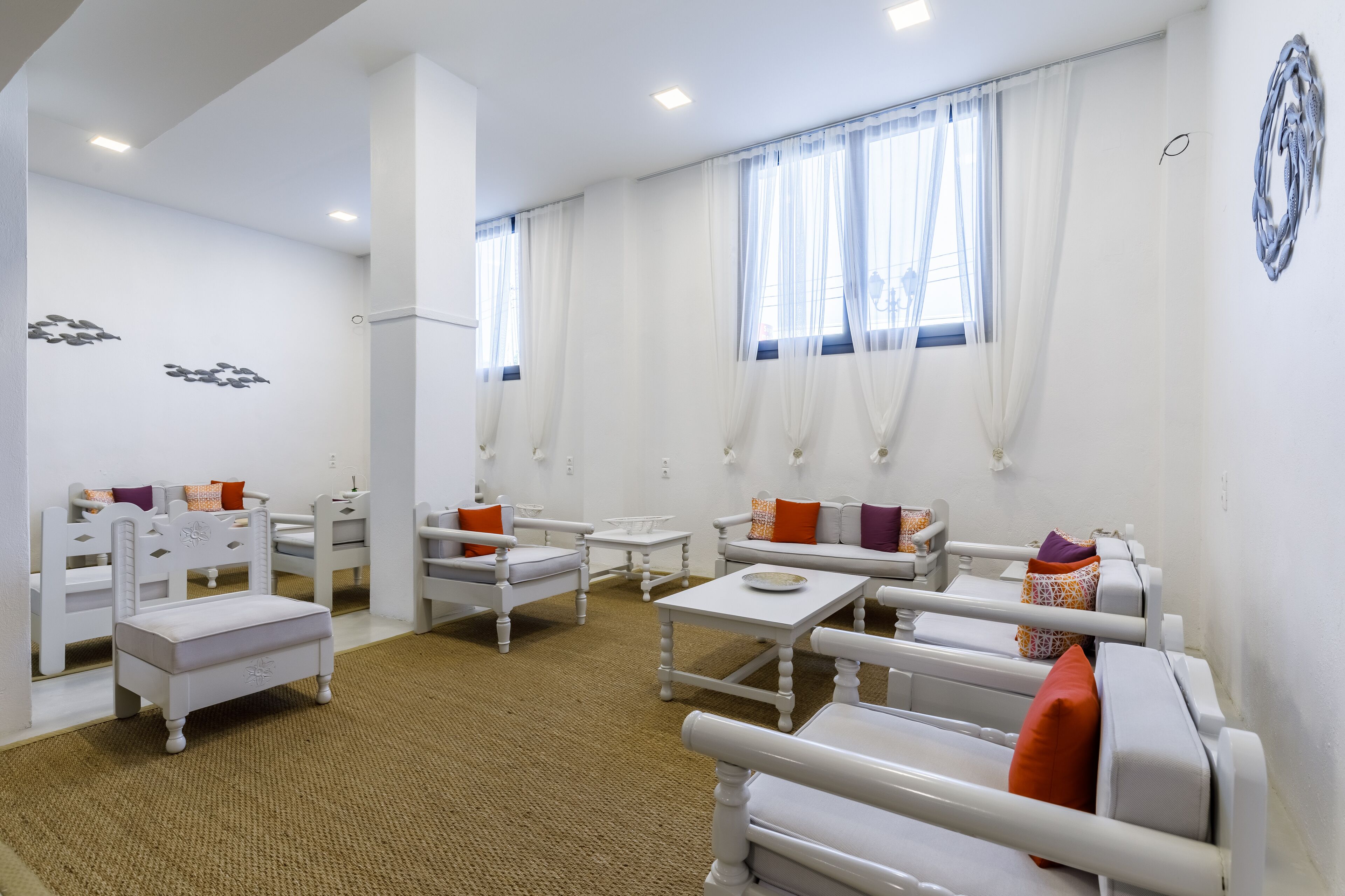 A bright, well-lit room with white furniture, including sofas and a small table, arranged around a central rug.