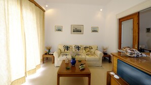 A living room with a sofa, a coffee table with a vase, and framed pictures on the wall. - Corali Hotel (Milos)