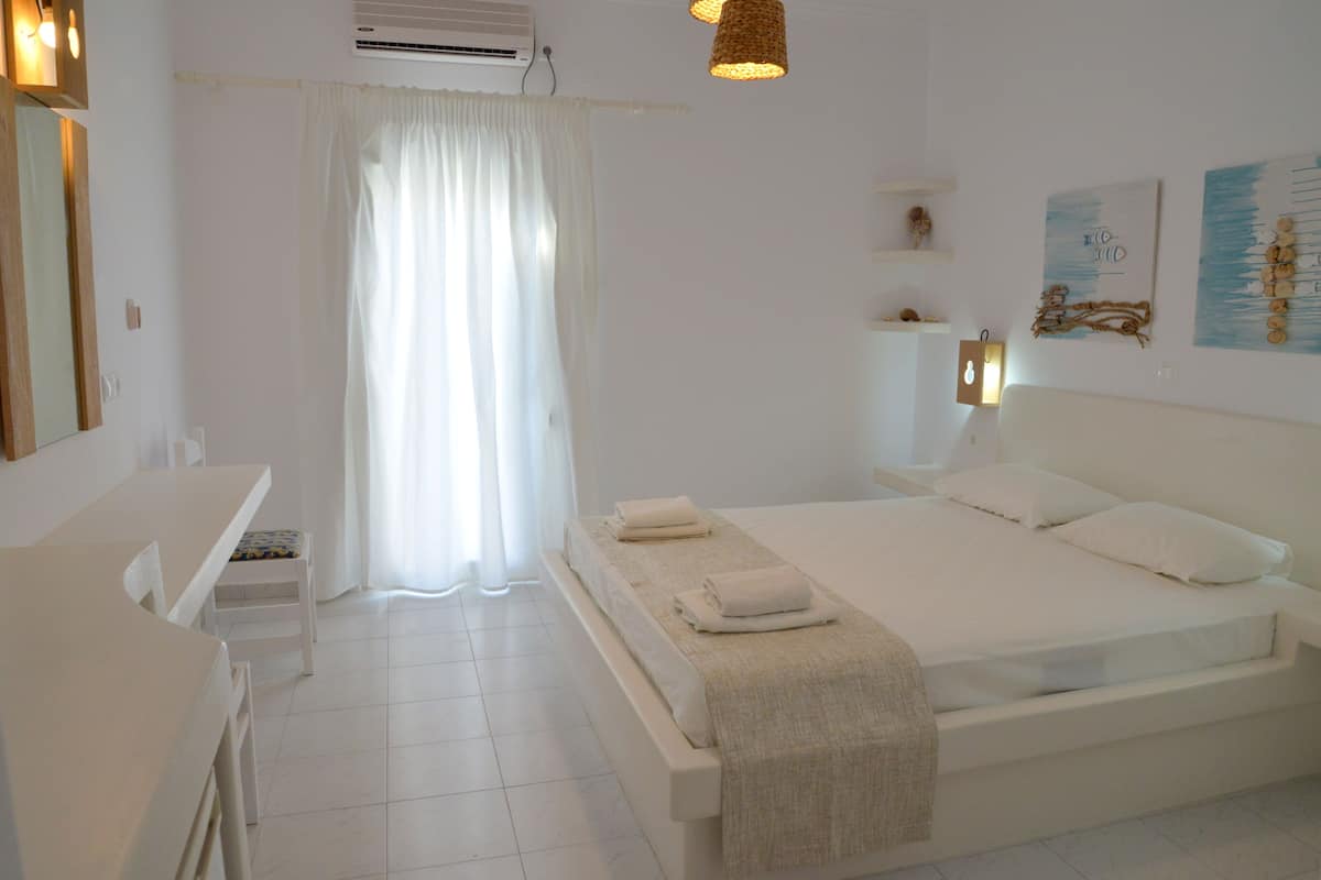 A clean, white bedroom with a bed, bedside tables, and a window with curtains.