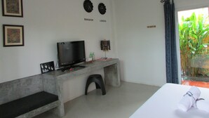 A modern hotel room with a flat-screen TV, a small desk with a computer, a bed with a rolled towel, and a view of greenery through the window. - The Park Drive-Thru Check-In Resort (Thanyaburi)