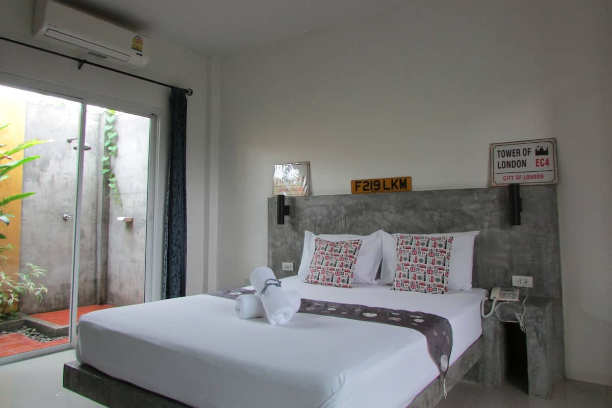 A hotel room with a bed, pillows, a bedside table, a phone, and a sign indicating the room number.