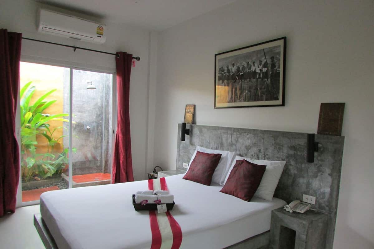 A hotel room with a bed, a nightstand, a telephone, a framed picture on the wall, and a sliding glass door leading to a balcony.