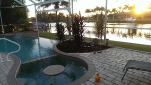 A swimming pool with a curved edge, surrounded by a paved deck and palm trees. - Villa Retreat - Exquisite Gulf Access (Cape Coral)