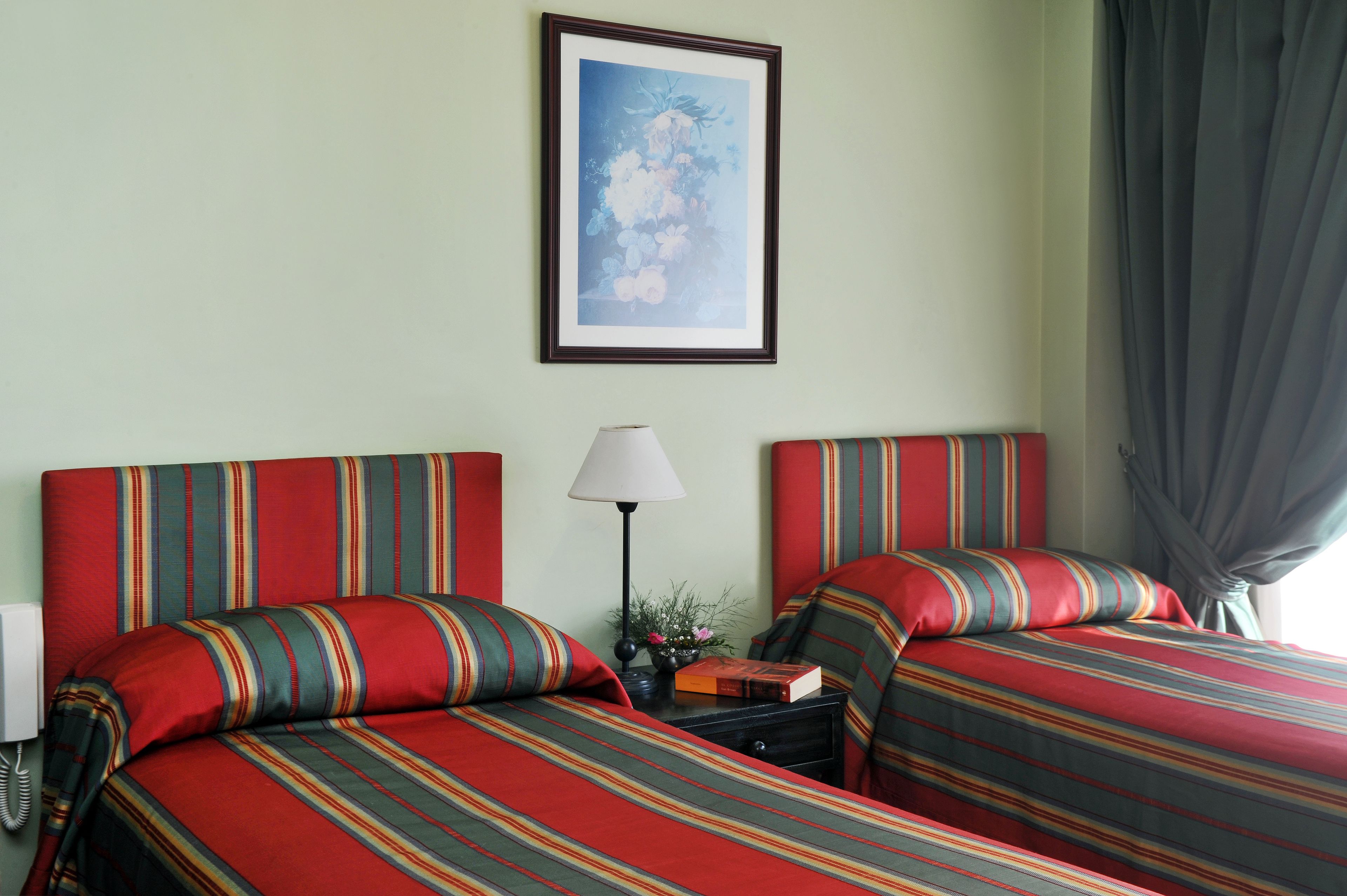 Une chambre d’hôtel avec deux lits, une literie à rayures, un tableau encadré au mur, une lampe de chevet et un téléphone.