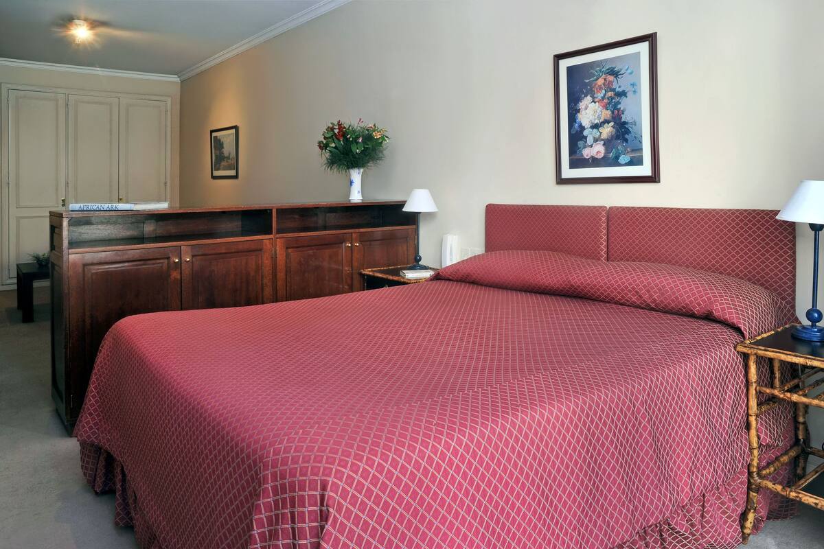 Une chambre à coucher avec un grand lit, une commode en bois, un vase de fleurs et un tableau encadré au mur.