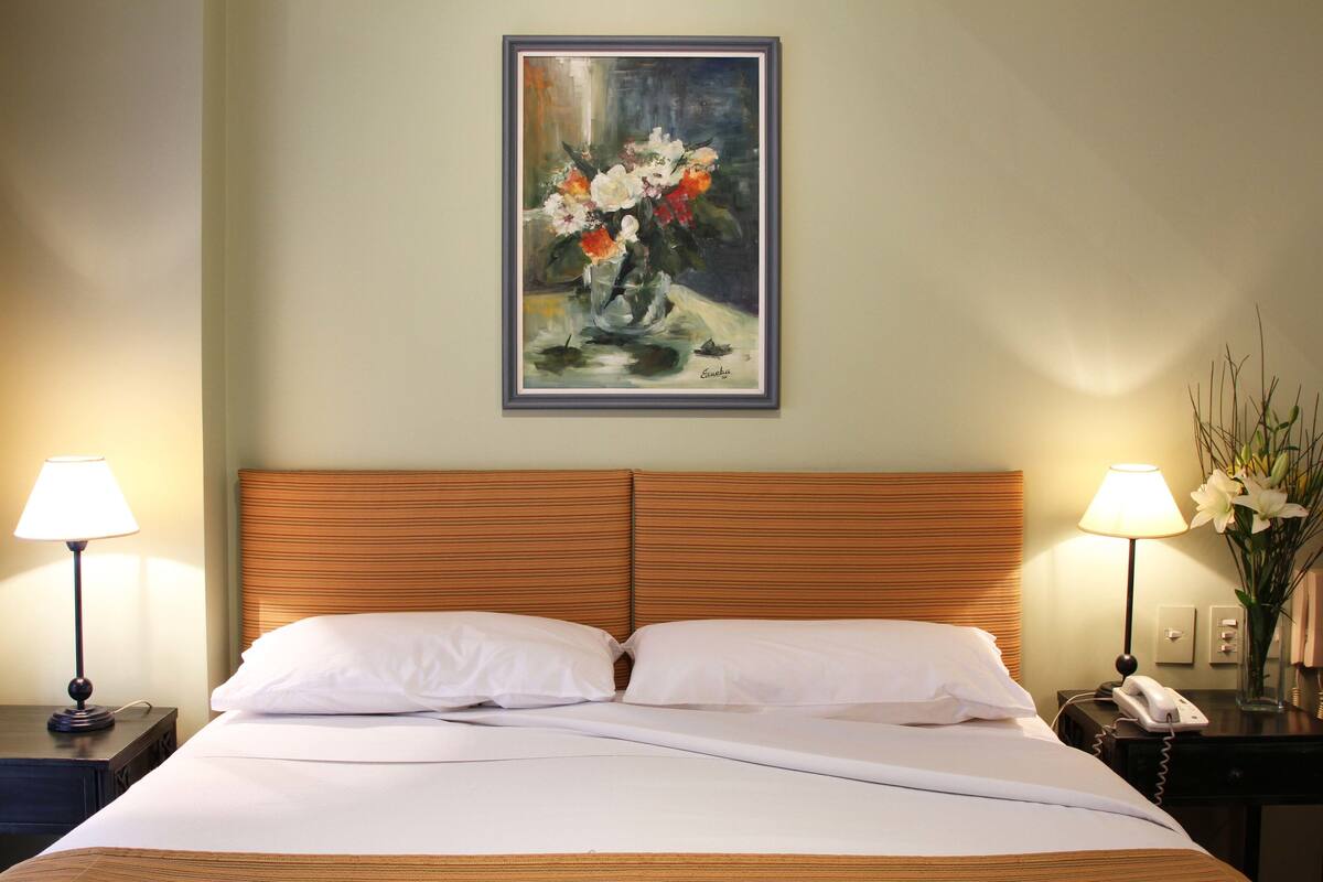 Une chambre d’hôtel avec un lit, deux lampes de chevet, une table de chevet avec un téléphone et un tableau au mur.
