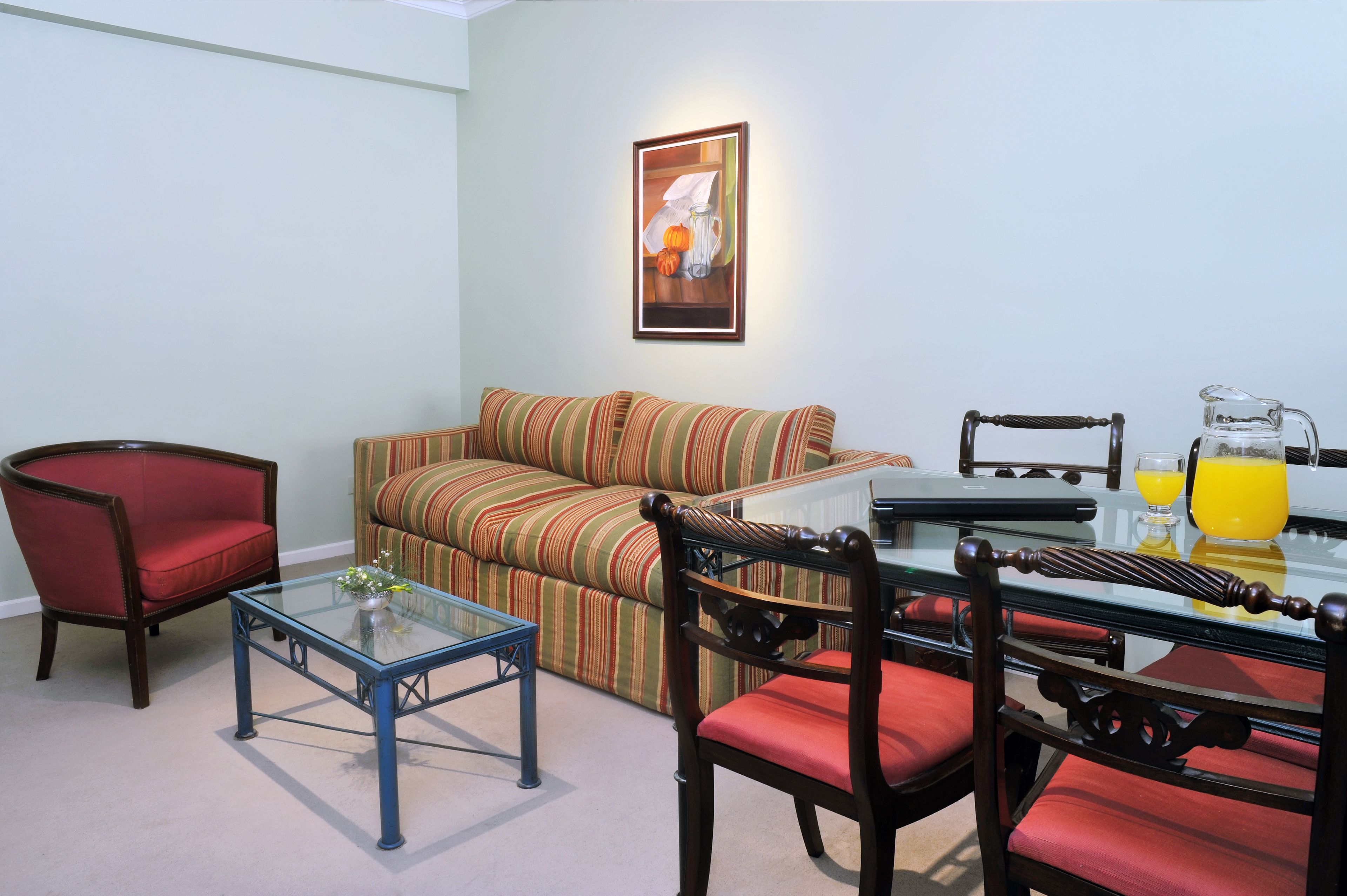 A living room with a glass coffee table, striped sofa, and a dining table with chairs.