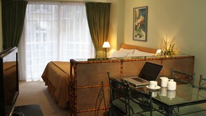 Una habitación de hotel con una cama, un escritorio con una computadora portátil, una silla, una mesa con tazas y un cuadro en la pared.