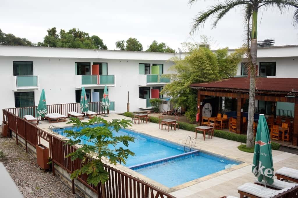 A pool area with lounge chairs and umbrellas, a bar area with tables and chairs, and a building with multiple balconies and windows.