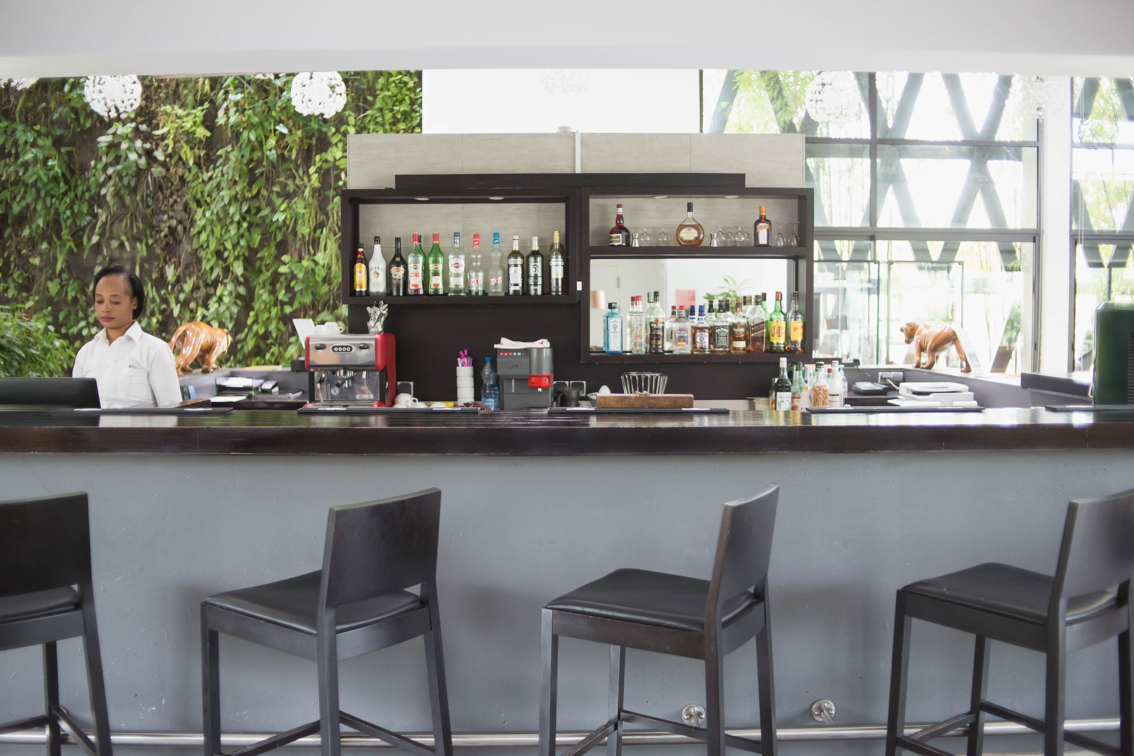 Zona de bar con mostrador, taburetes y estantes con botellas.