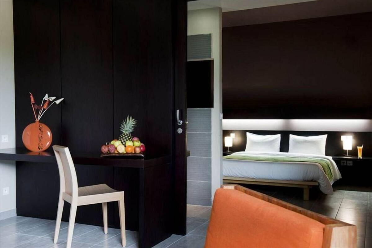 Une chambre d’hôtel avec un lit, une table de chevet, une chaise et un bureau avec des fruits.
