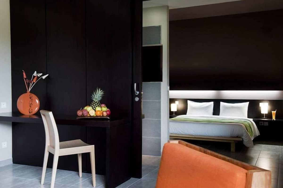 Una habitación de hotel con cama, mesita de noche, silla y escritorio con fruta.