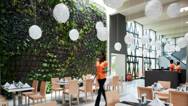 Un restaurant modern amb seients interiors, una paret verda i lluminàries esfèriques penjants.