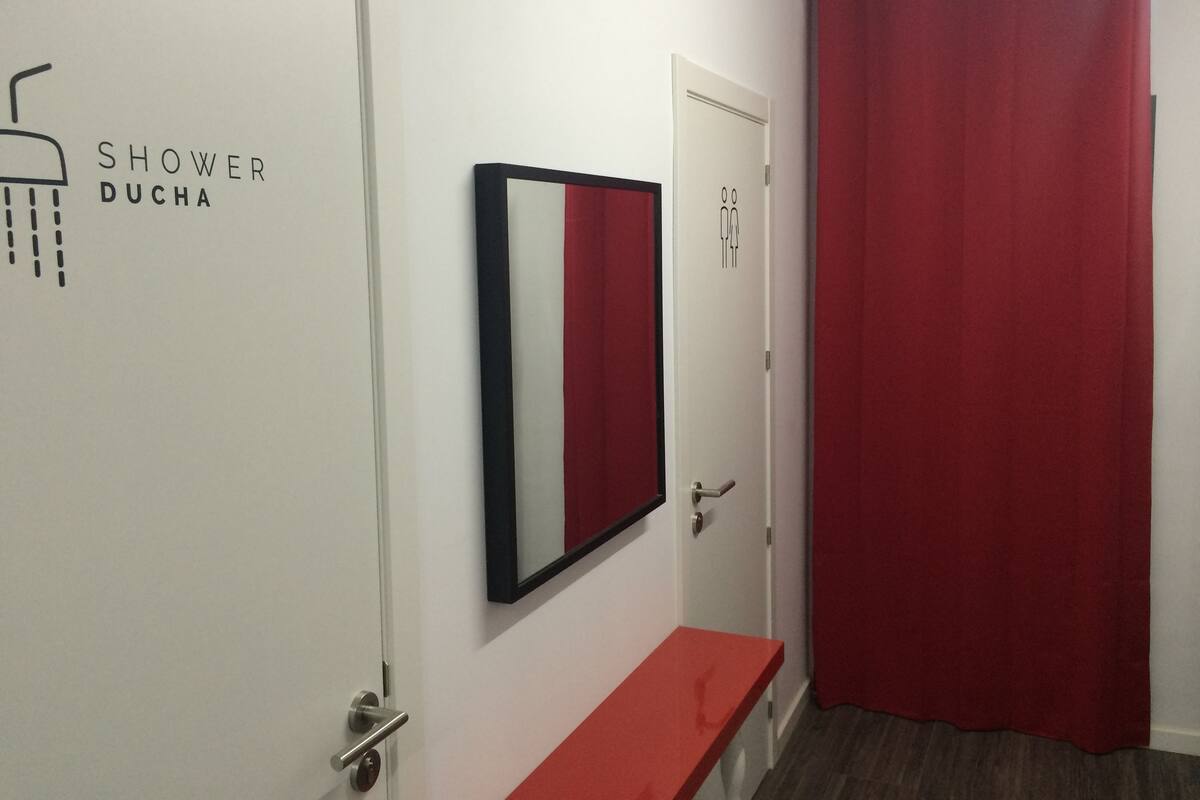 A bathroom with a shower labeled 'SHOWER DUCHA', a mirror, and a red curtain.