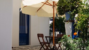 Un patio con una mesa y sillas bajo una sombrilla blanca, rodeado de muros blancos y contraventanas azules.