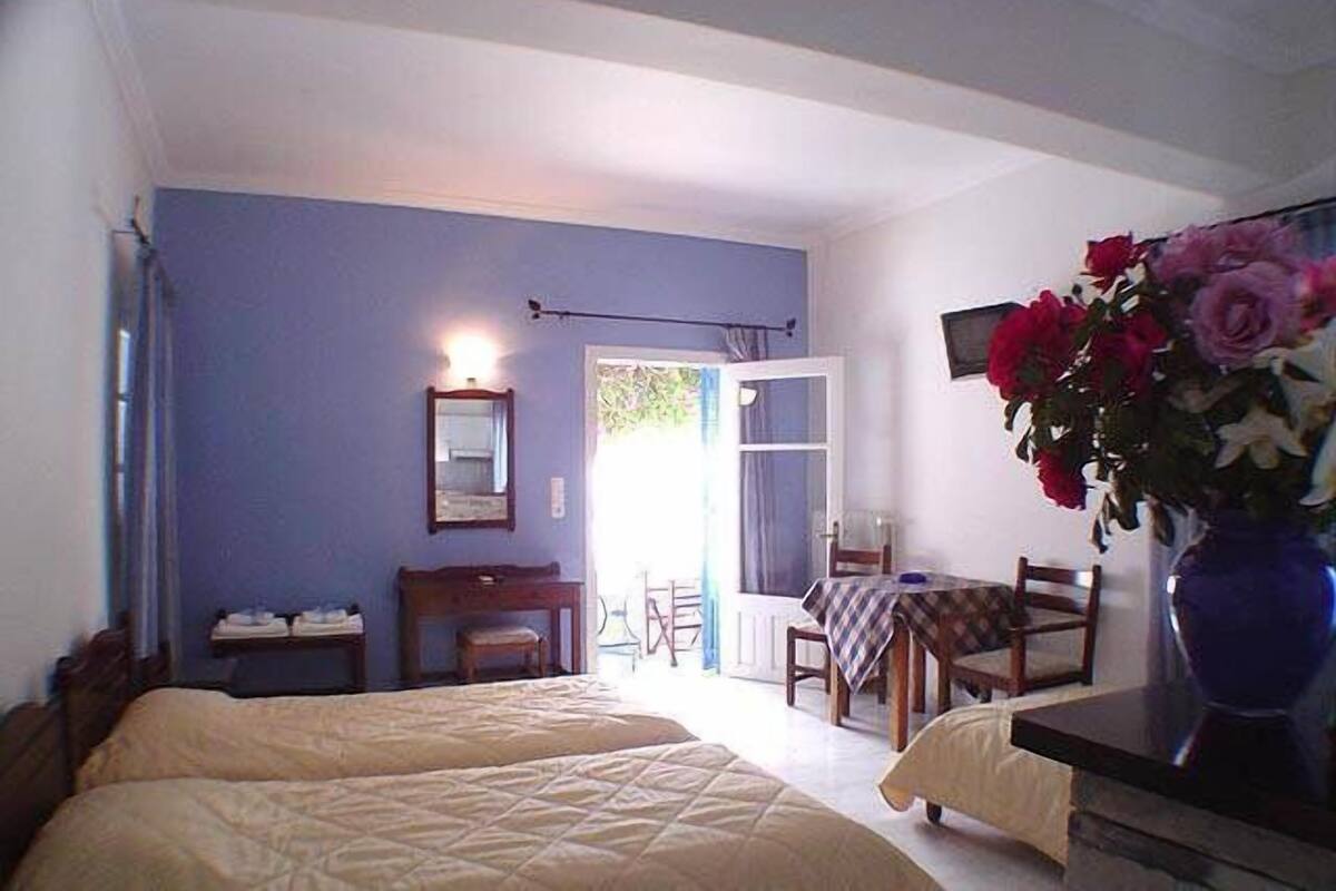 A bedroom with two beds, a small table, a chair, and a vase with flowers.