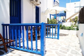 A narrow street with white buildings and blue doors, a stone-paved path, and outdoor seating with umbrellas. - Giannis Hotel Apartments (Milos)