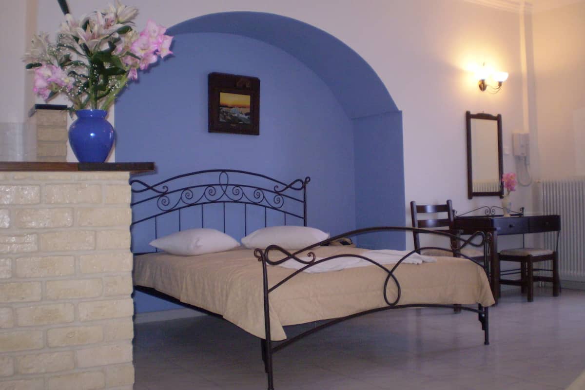 A bedroom with a bed, a chair, a desk, a vase with flowers, and a picture on the wall.