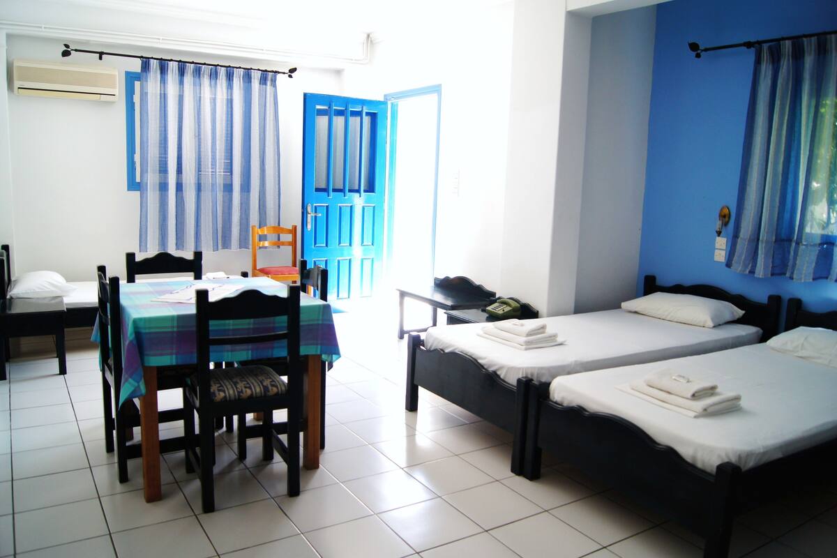 A room with two beds, a dining table with chairs, and a blue door.