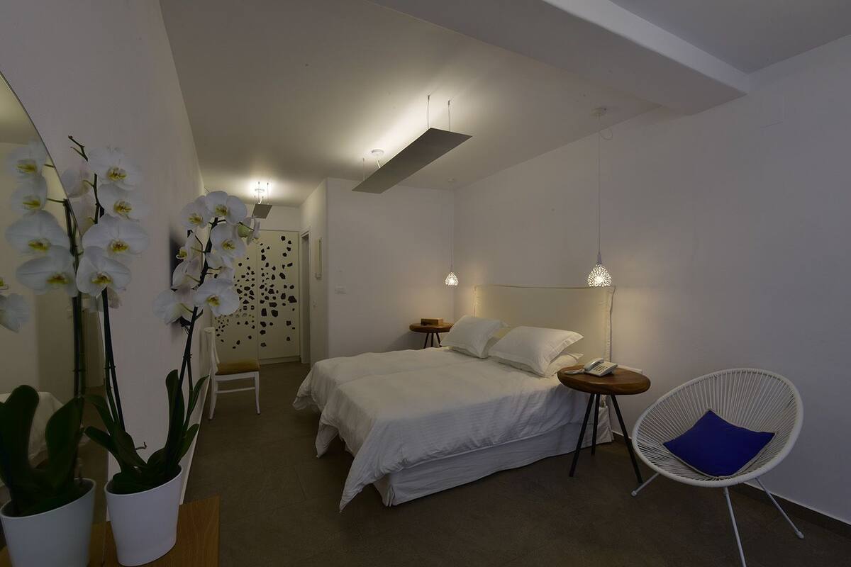 Un dormitorio moderno con cama, mesitas de noche, una silla y orquídeas decorativas.