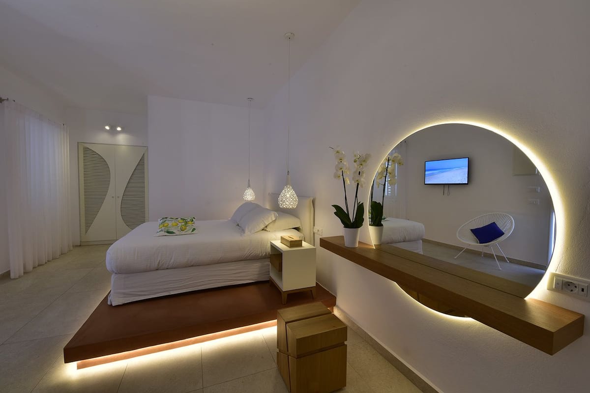 Un dormitorio moderno con cama, mesitas de noche, espejo y televisor.