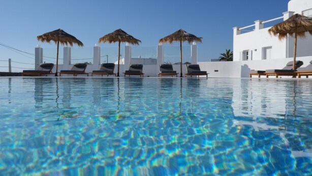 Ein klares Schwimmbecken mit Liegestühlen und Sonnenschirmen, umgeben von weißen Gebäuden.