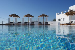 A clear pool with lounge chairs and umbrellas, surrounded by white buildings. - Margie Mykonos Hotel (Mykonos)