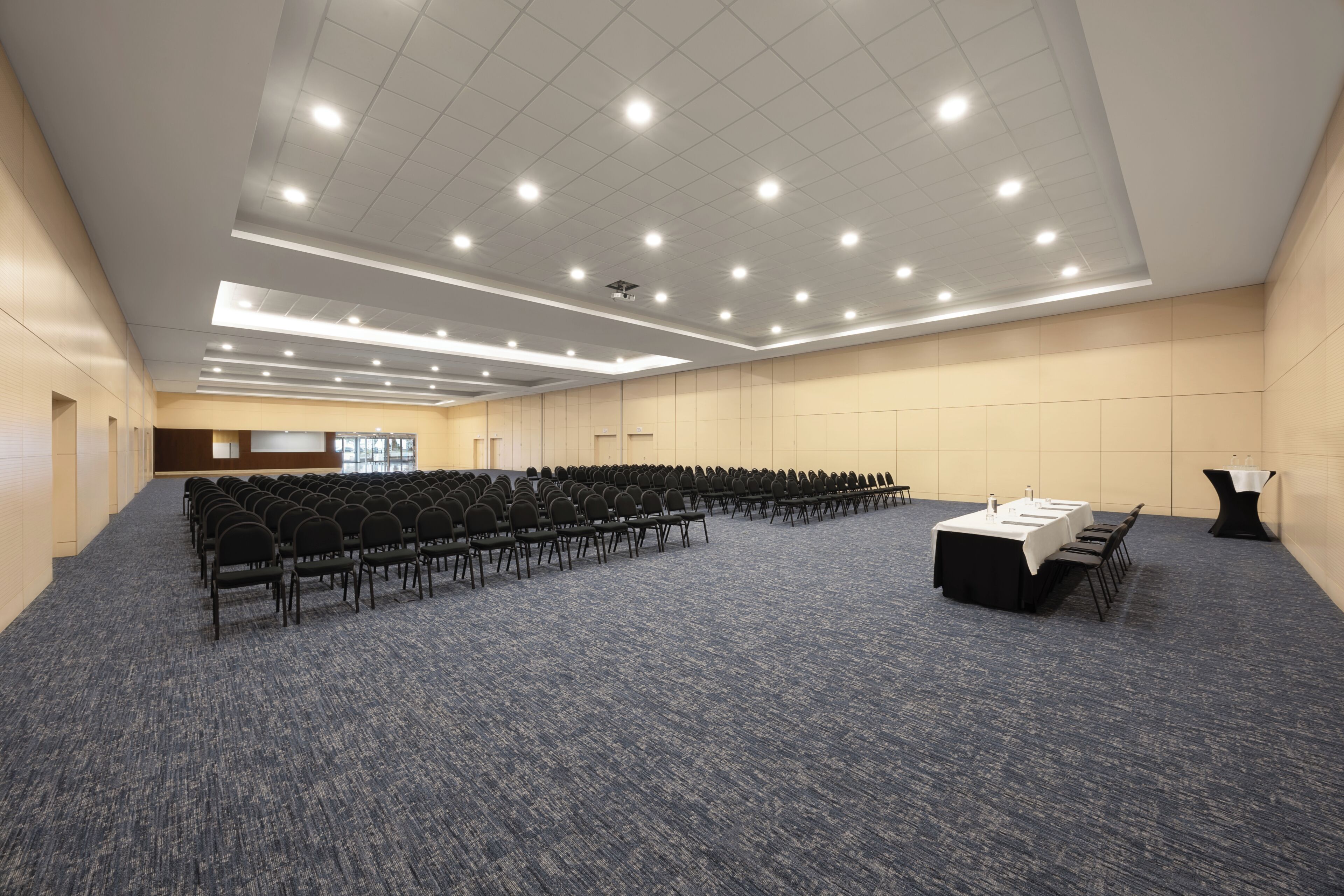 A conference room with rows of chairs, a long table, and a carpeted floor.