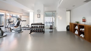 A gym with exercise equipment, a rack of dumbbells, and a wooden cabinet with towels.