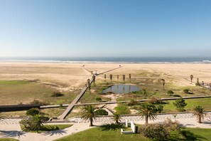 An aerial view of a coastal park with pathways, palm trees, a small pond, and a beach in the background. - Eurostars Oasis Plaza Hotel (Figueira da Foz)